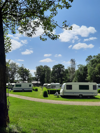 Campinggelände mit mehreren Wohnwagen auf grünen Stellplätzen unter blauem Himmel mit Wolken.