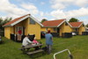 Modern yellow cabins with red roofs and a family sitting outside enjoying a meal.