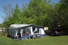 Wohnwagen mit Vorzelt auf einem grünen Stellplatz, umgeben von Bäumen auf dem Ringkøbing Campingplatz
