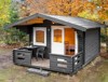 Charming grey camping cabin with covered terrace, surrounded by autumn trees.