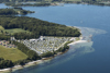 Dronefoto af Sandskaer Strandcamping, der viser campingpladsens smukke placering ved Genner Bugt med stille vand. Halvøen Kalvø og Nørreskoven øst for campingpladsen ses også på billedet.