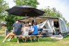 Familie sidder ved et campingvognstelt med markise på Nymindegab Camping.