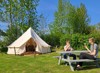 They are sitting and eating ice cream next to a glamping tent, where there are seats and good shelter from the fields by the trees.